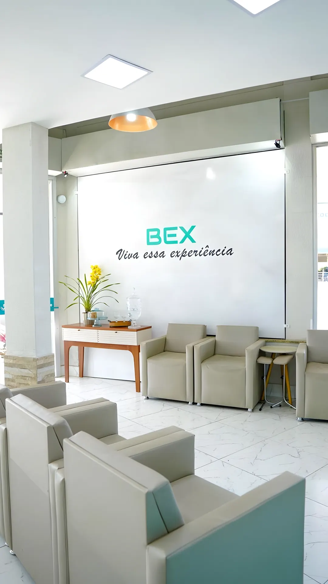 Recepção da BEX com a parede "BEX — Viva essa experiência" e poltronas claras